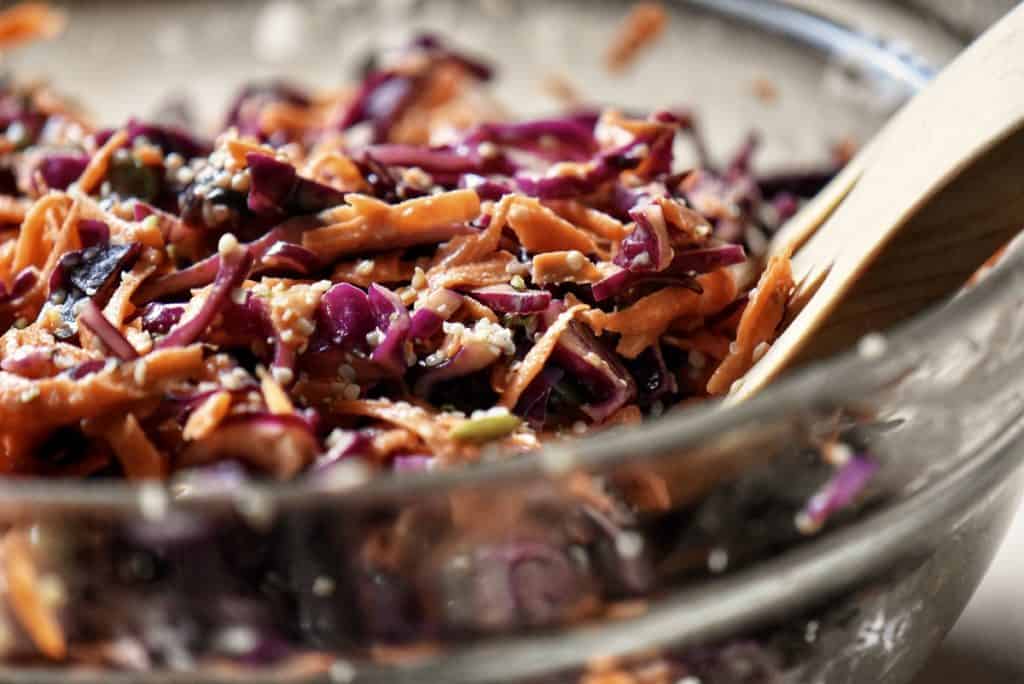 A close up of red cabbage slaw in a glass bowl.