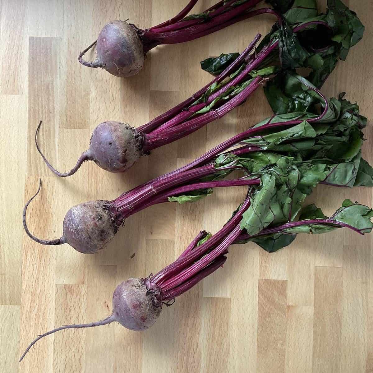 Fresh red beets with beet greens still attached on a cutting board.