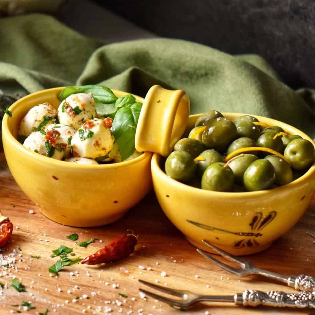 Marinated mozzarella balls and olives in a yellow dish.