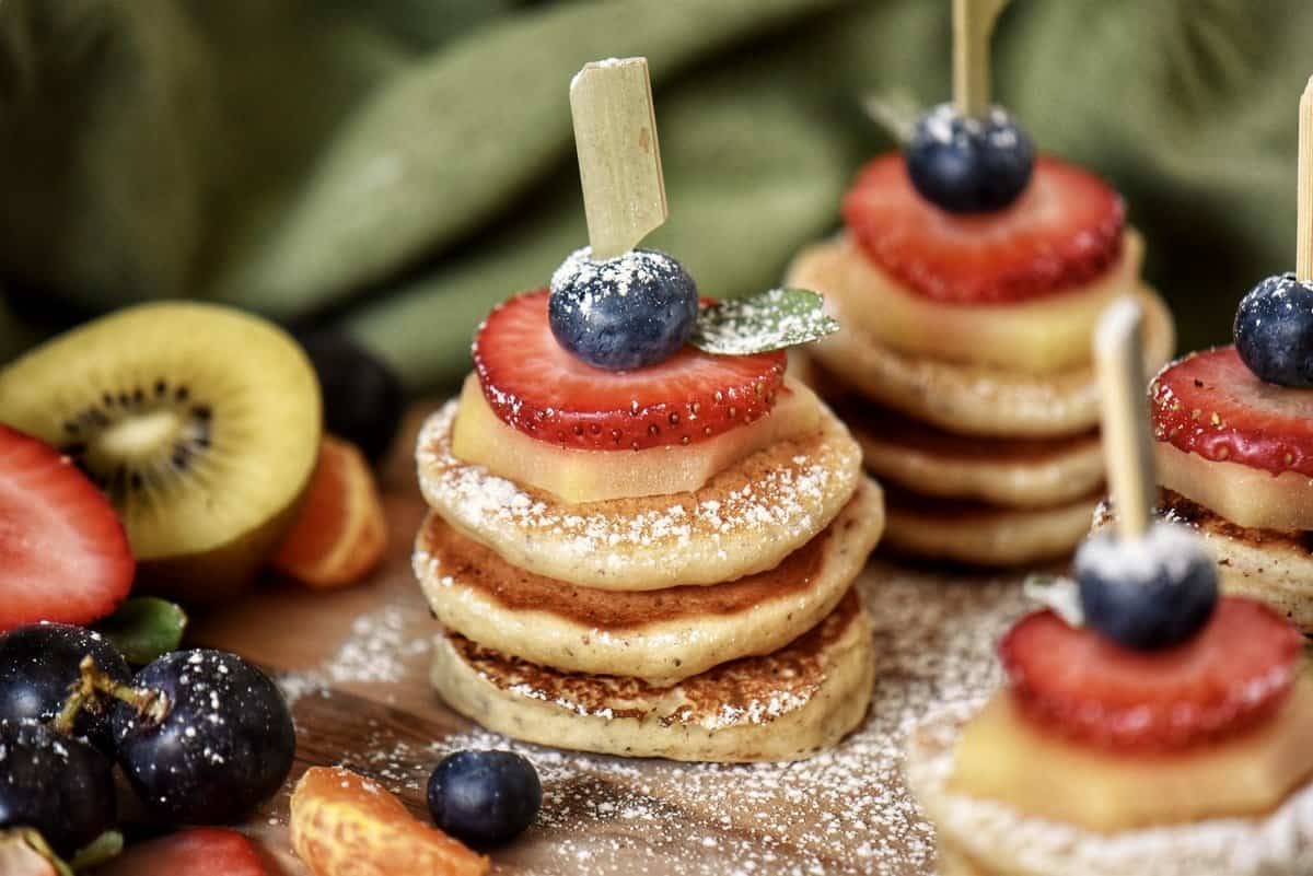 A stack of three mini pancakes surrounded by fresh fruit.