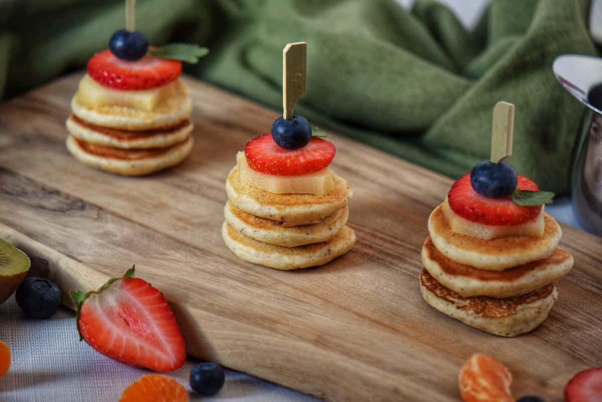 Stacks of mini pancakes on a wooden board.
