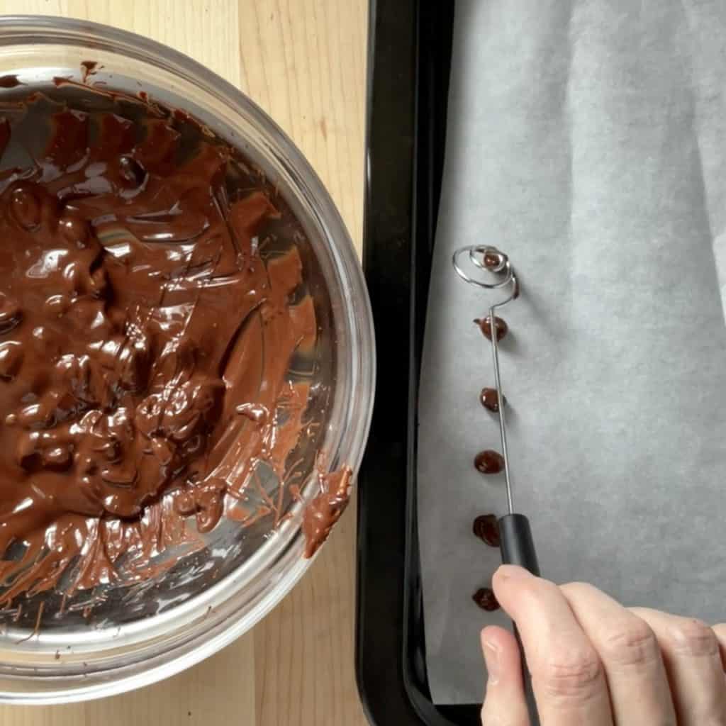 Chocolate coffee beans being transferred to a parchment lined tray.