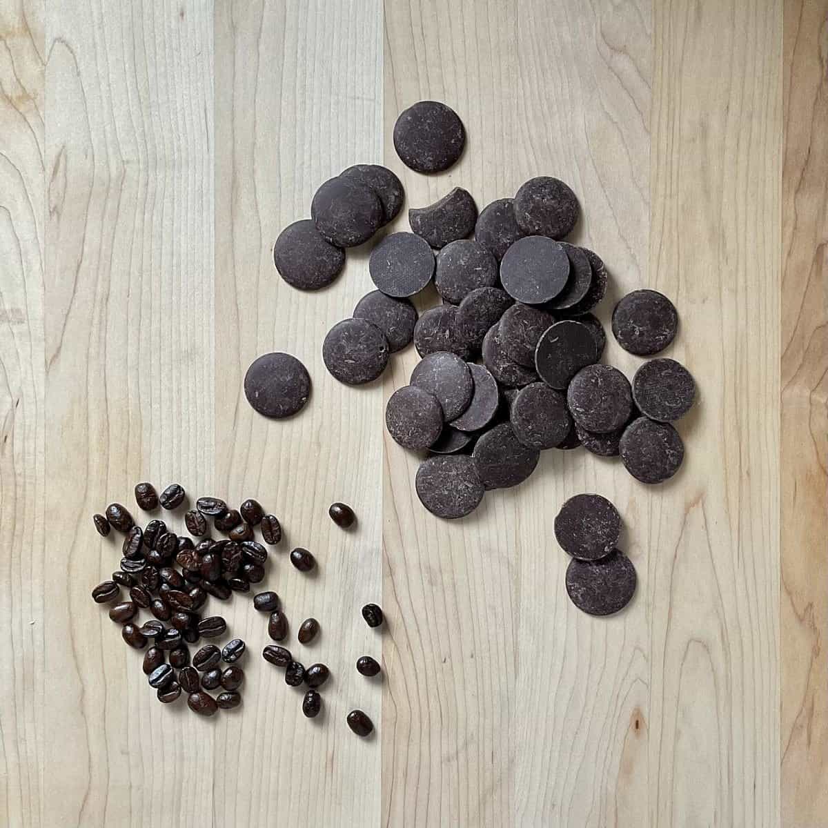 Whole espresso beans and dark chocolate discs on a wooden board.