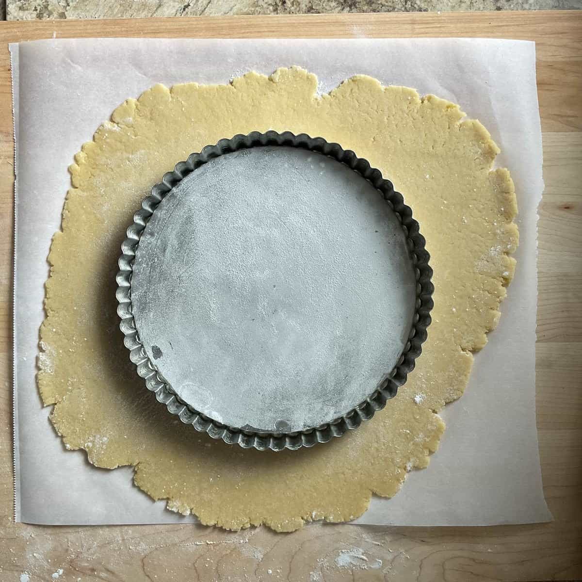 A round tart pan on a rolled out sweetcrust dough.