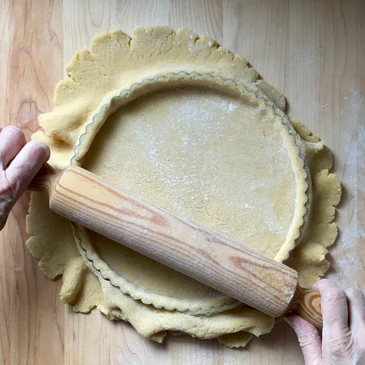 A rolling pin is gently rolling over the top of the tart case to trim away the excess dough.