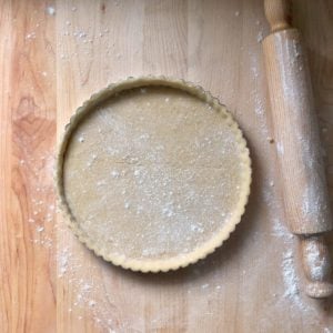 Pasta frolla in a tart pan, next to a rolling pin.