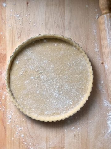 Pasta frolla in a tart pan, next to a rolling pin.