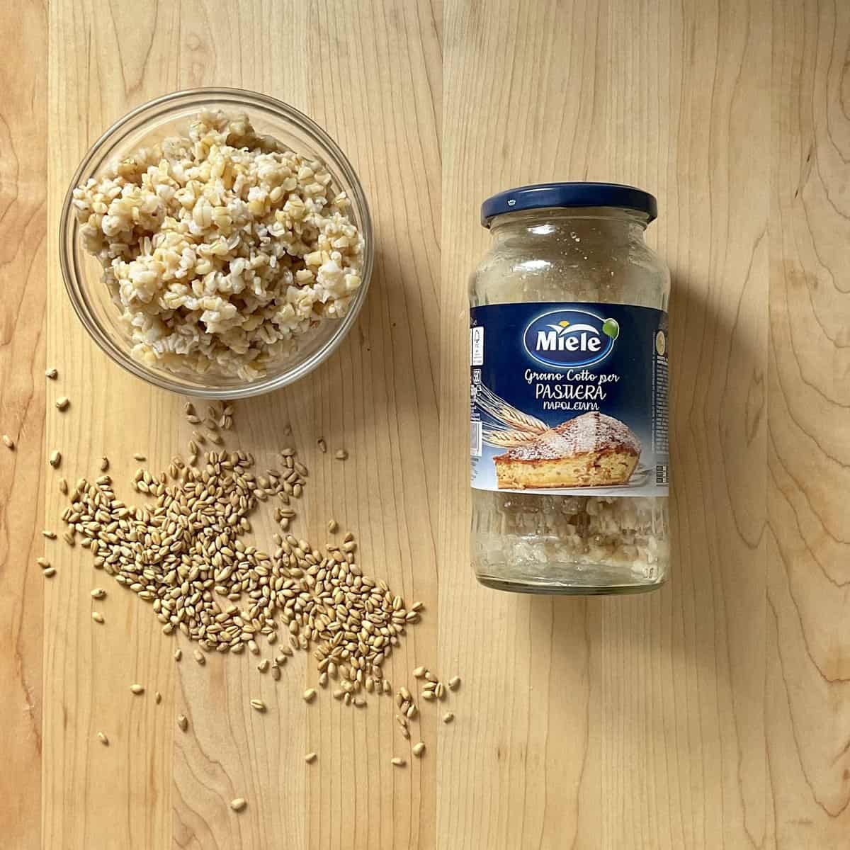 A bottle of pre-cooked wheat berries next to the grains on a wooden board. 