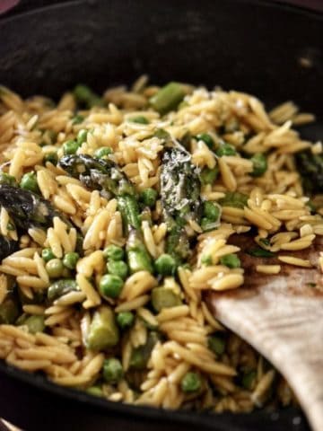 Orzo risotto combined with spring peas and asparagus in a pan.