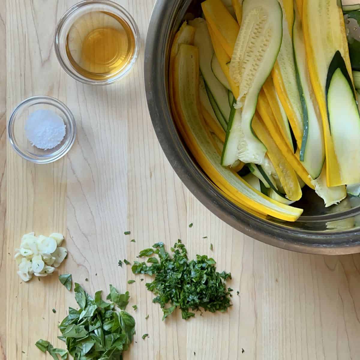Sliced zucchini in a colander, next to chopped herbs.