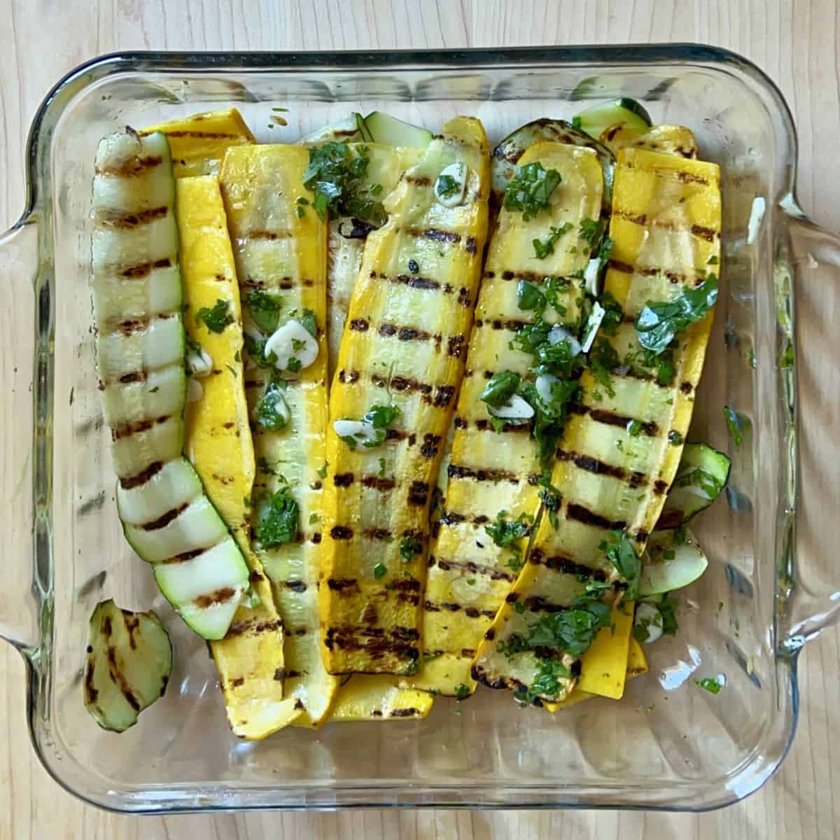 Grilled zucchini being marinated in a dish.