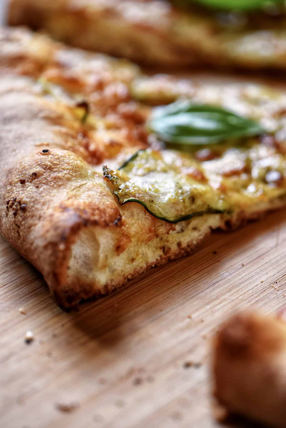 A slice of pizza with zucchini and basil pesto on a cutting board.