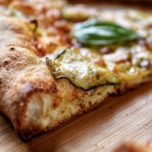 A slice of zucchini pizza on a wooden board.