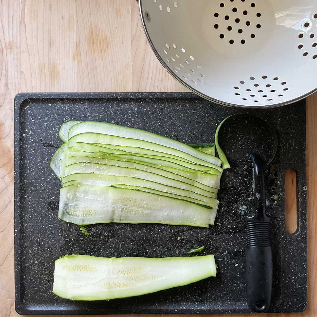 Sliced zucchini ribbons on a cutting board.