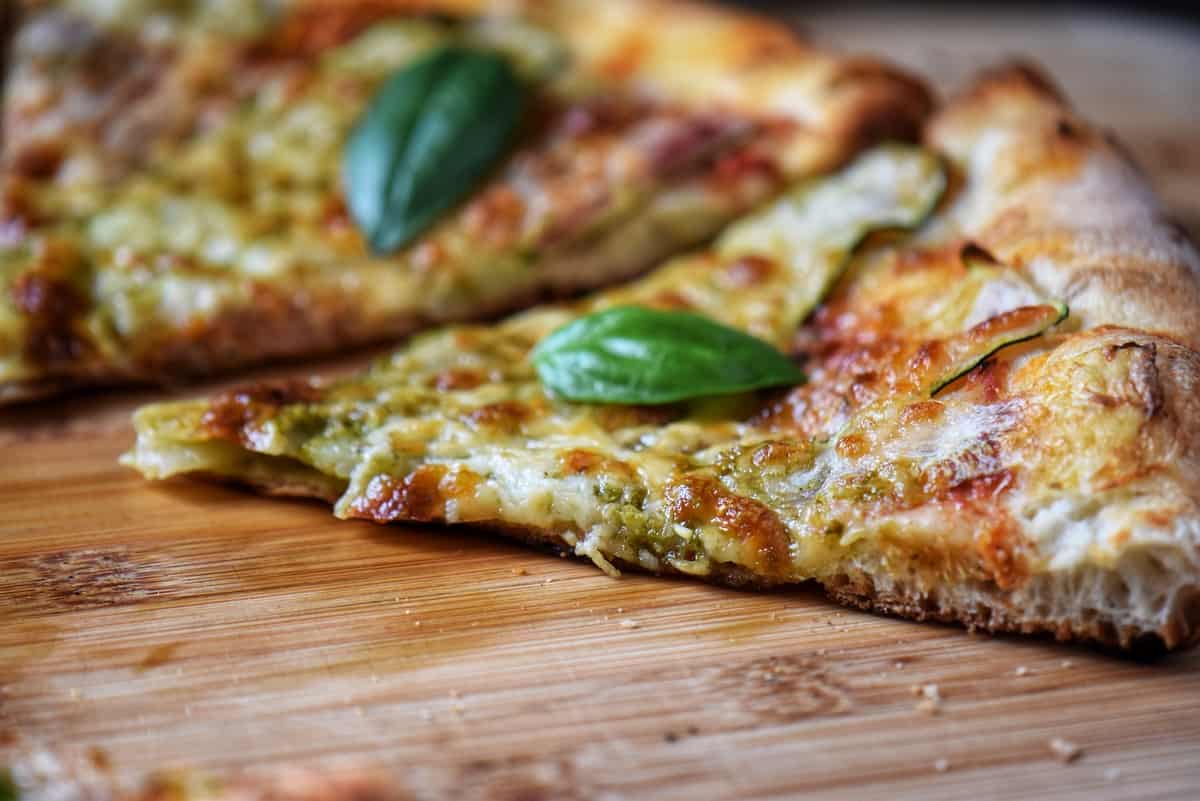 A slice of pizza with zucchini and basil pesto on a cutting board.