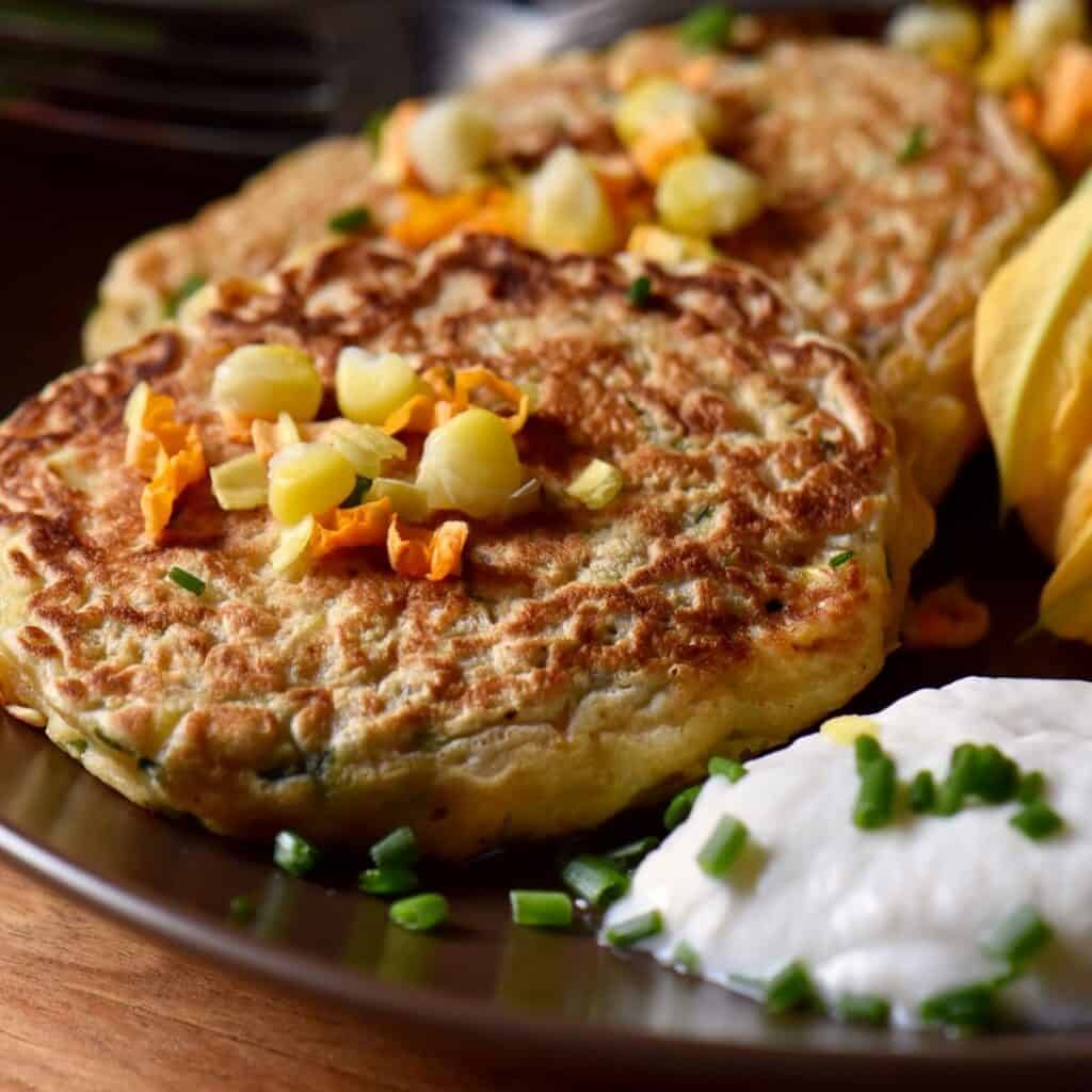 Zucchini pancakes on a plate next to garlic yogurt sauce.
