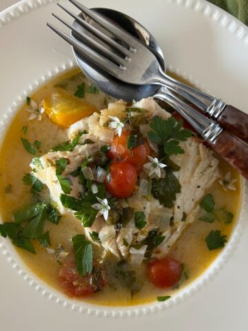 An overhead photo of poached codfish in an herb tomato broth.