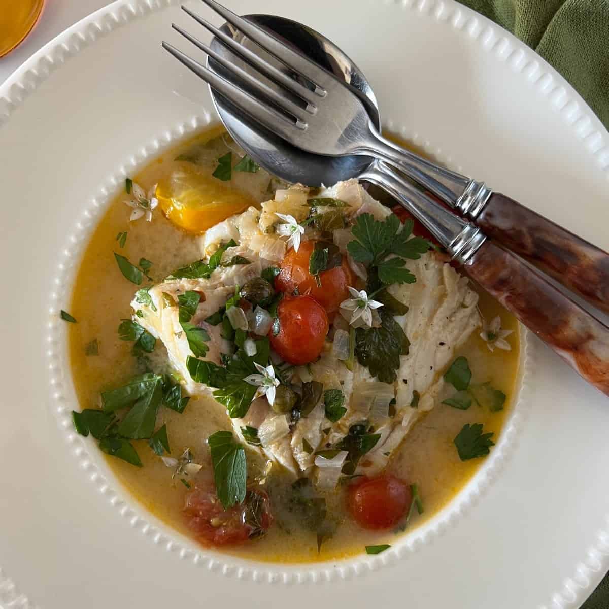 An overhead photo of poached codfish in an herb tomato broth.