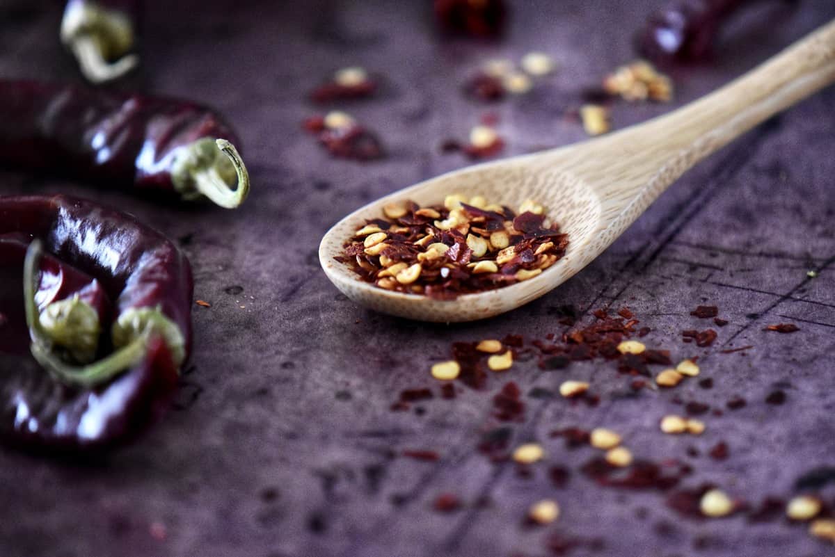 A spoonful of chili flakes next to dry chili peppers.