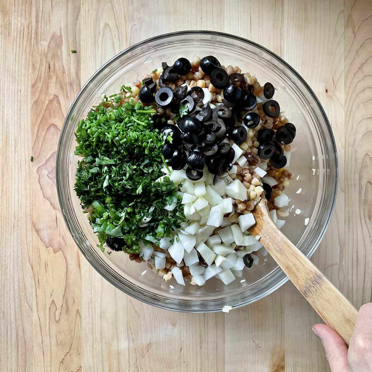 Chopped fresh herbs, olives and fennel in a bowl with fregola.