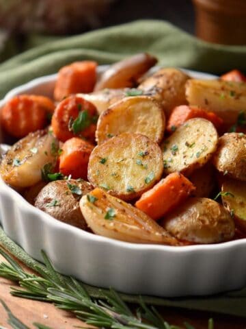 Roasted small potatoes and carrots in a white baking dish.