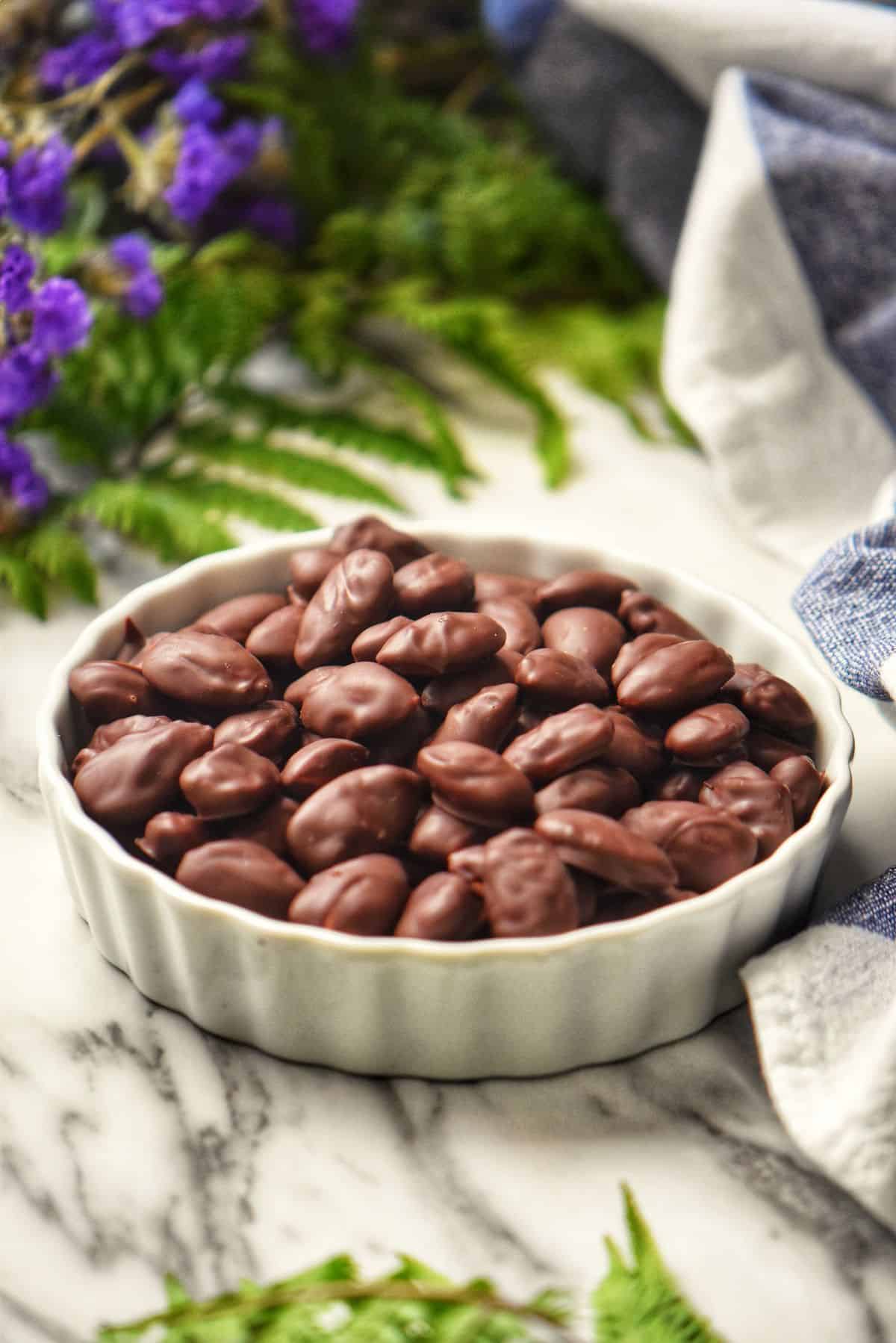 Chocolate covered almonds in a white bowl.