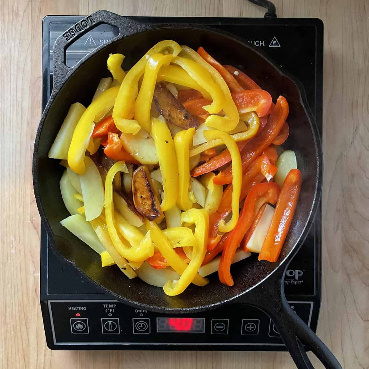 Sliced potatoes and peppers cooking in a cast iron pan.