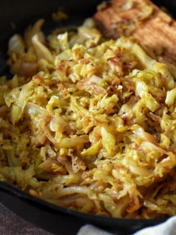 A close up photo of fried cabbage and onions in a cast iron pan.