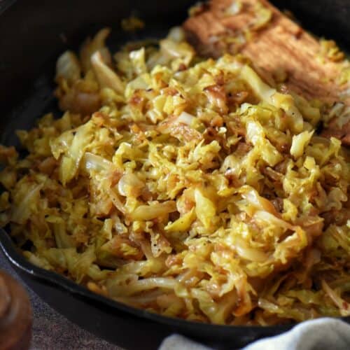A close up photo of fried cabbage and onions in a cast iron pan.