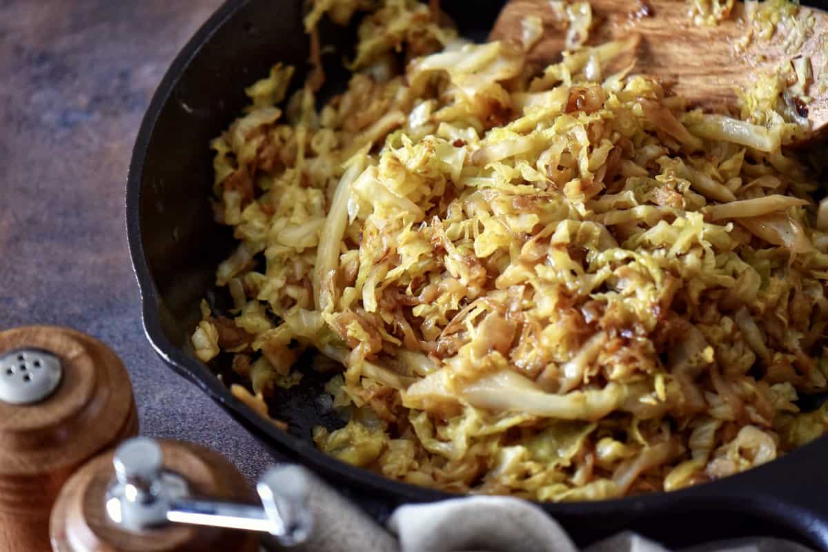 Fried cabbage next to a wooden salt and pepper shaker.