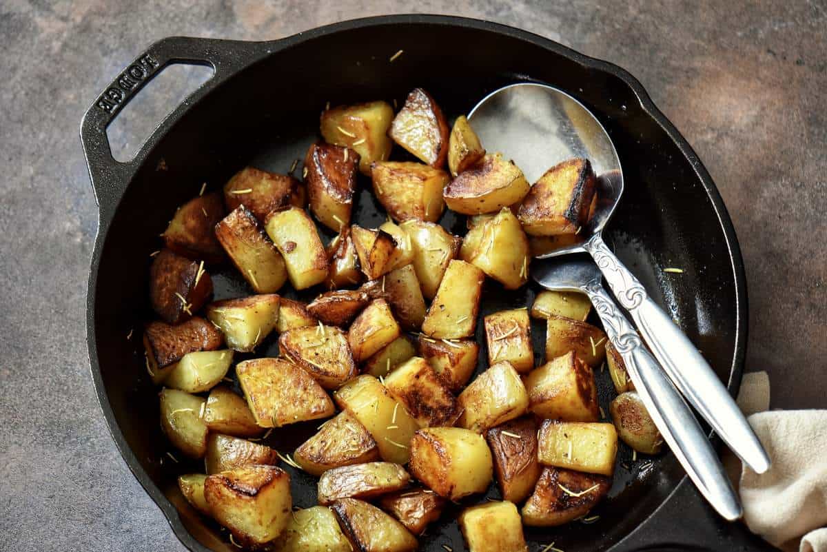 A metal spoon full of crispy, golden brown skillet potatoes.