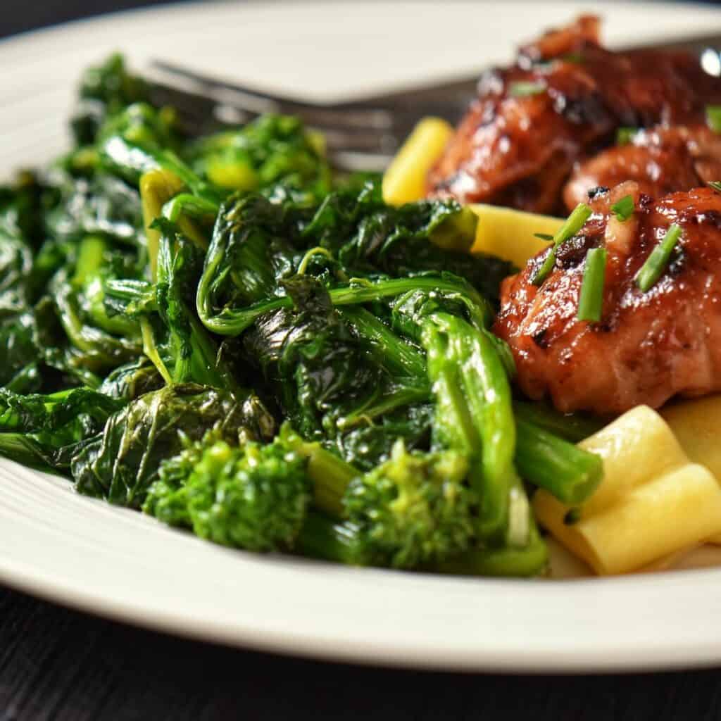 Rapini with chicken thighs on a white plate.