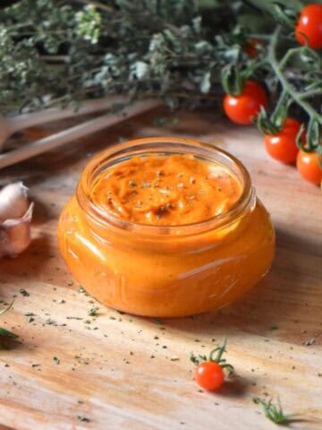 A jar of cherry tomato sauce surrounded by cherry tomatoes on a vine.