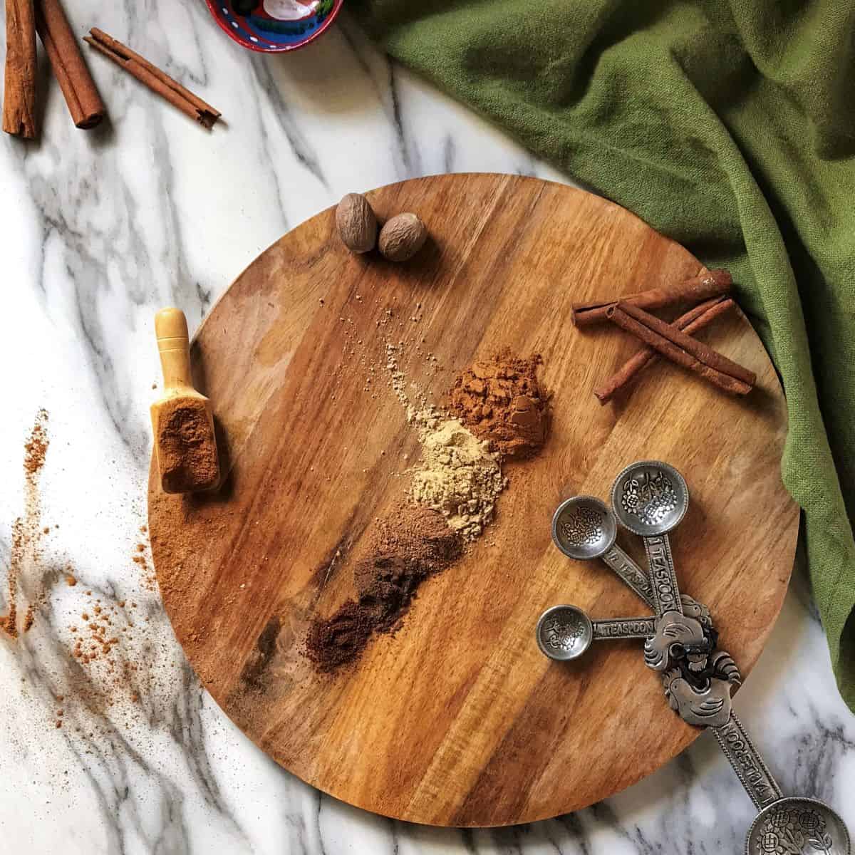 An overhead photo of ground spices like nutmeg, cinnamon and cloves on a wooden board.