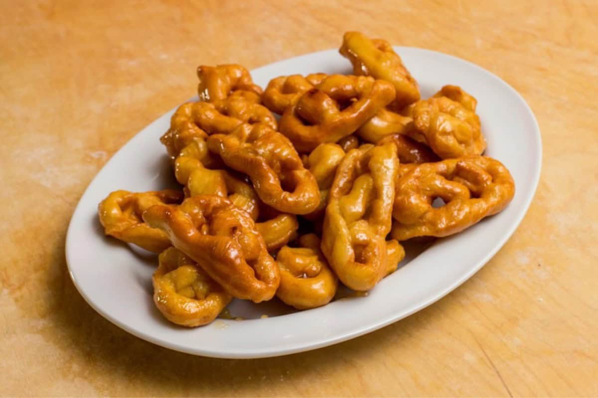 Honey coated Italian fritters called Caragnoli on a white platter.