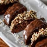 A close up photo of chocolate covered chocolate biscotti garnished with nuts, on a white dessert plate.