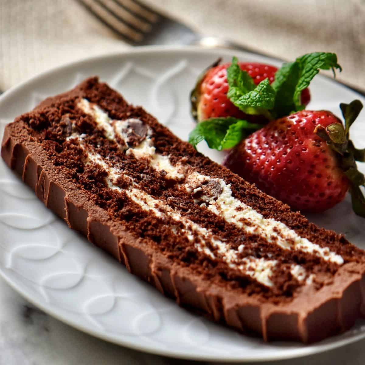 A slice of layered Chocolate Cake with ricotta cheese filling with strawberries on a white plate.