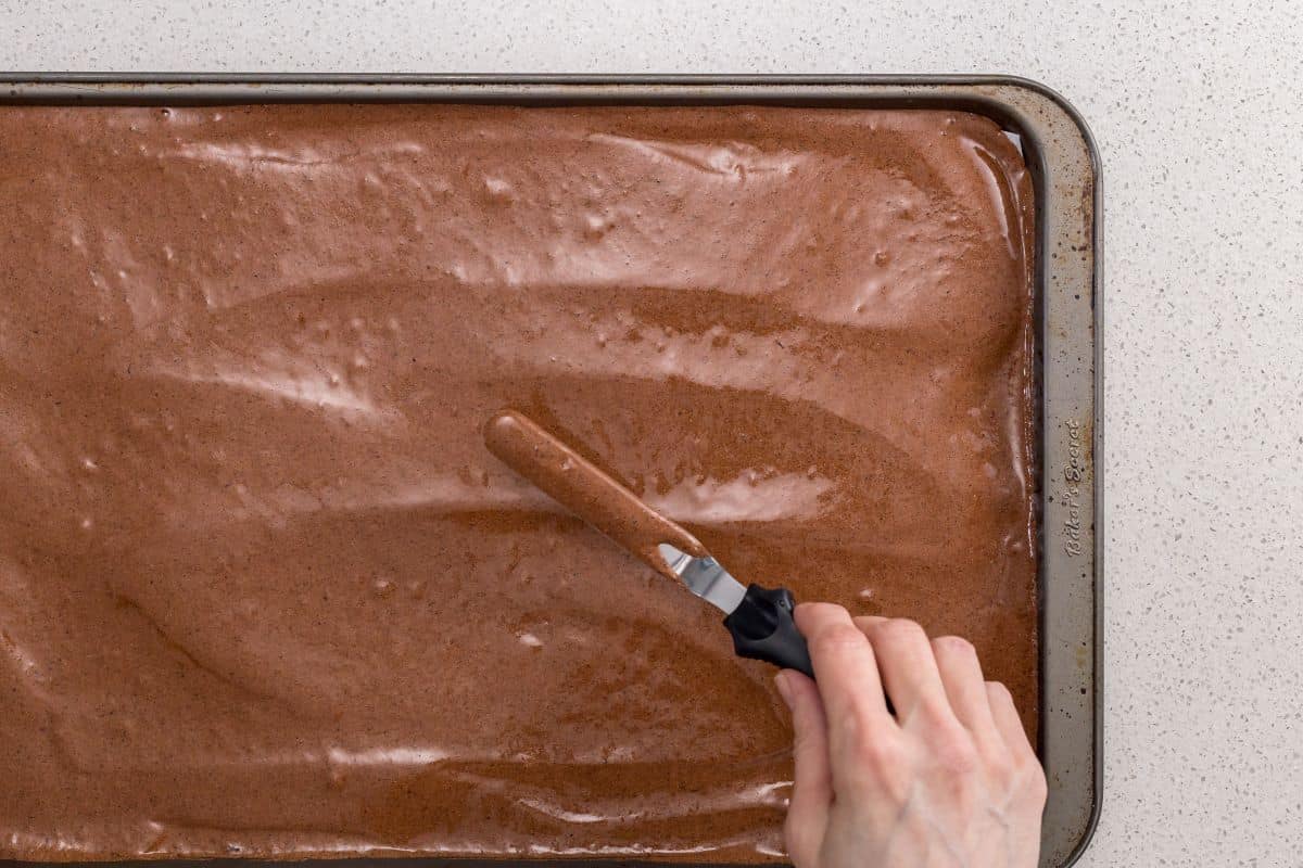 The chocolate batter is being spread evenly on the sheet pan.