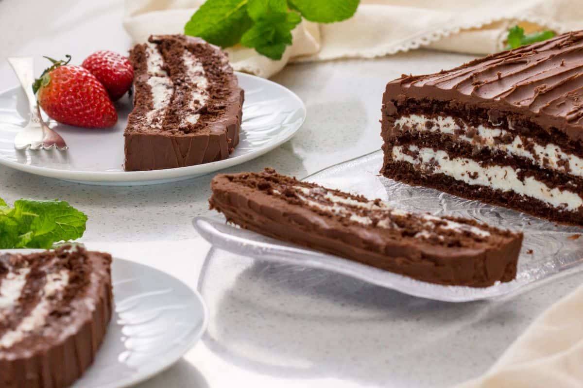 Slices of chocolate cream cake can be seen on white plates, served with strawberries.
