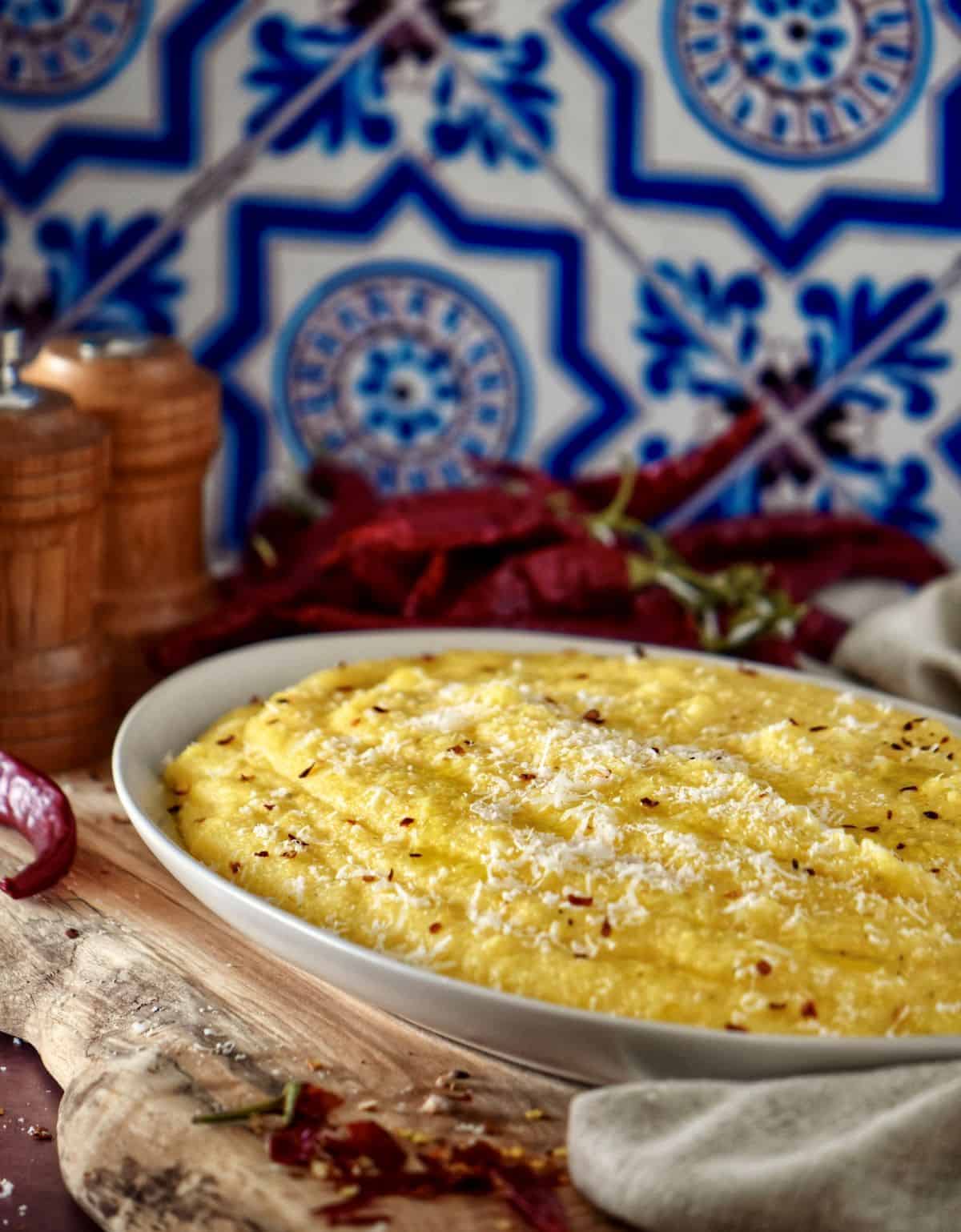 Cornmeal polenta in a white oval serving dish, topped with cheese, olive oil and crushed chili peppers.