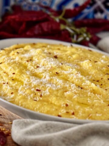 A platter of creamy polenta topped with a drizzle of olive oil and chili flakes.