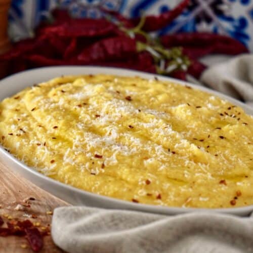 A platter of creamy polenta topped with a drizzle of olive oil and chili flakes.