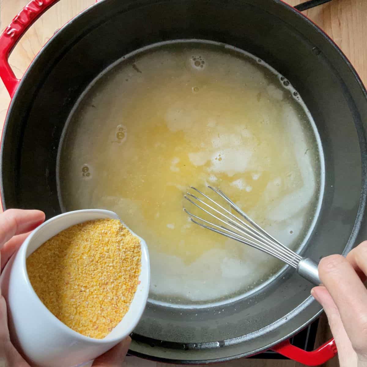 Polenta is slowly being poured in a pot of boiling water, ready to be whisked.