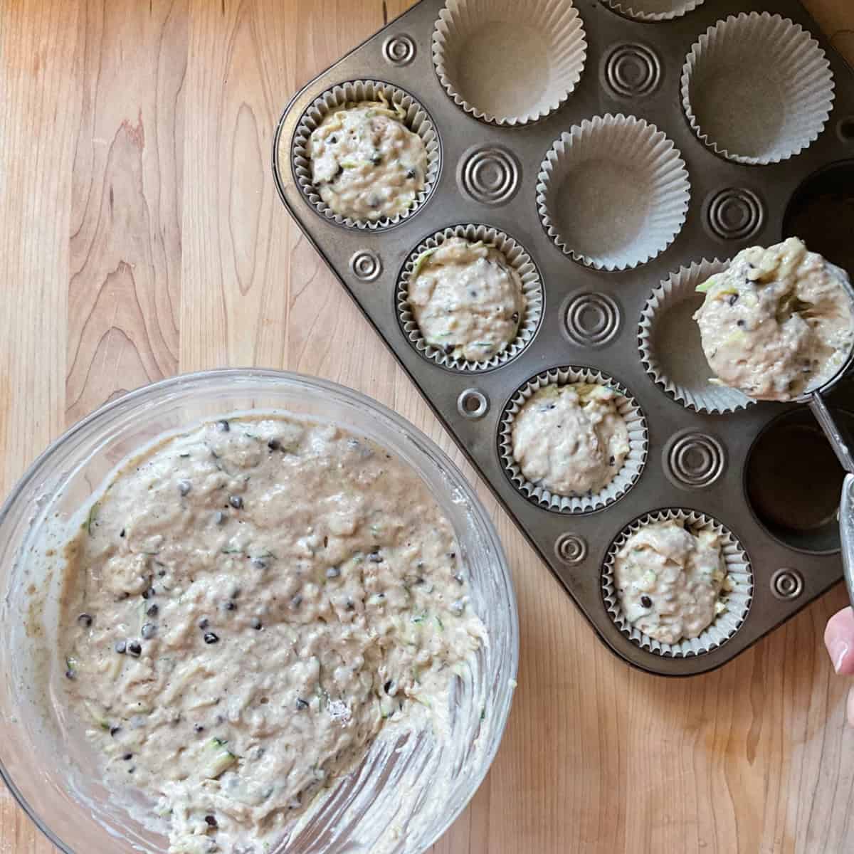 The zucchini muffin batter is being portioned in the muffin tins.