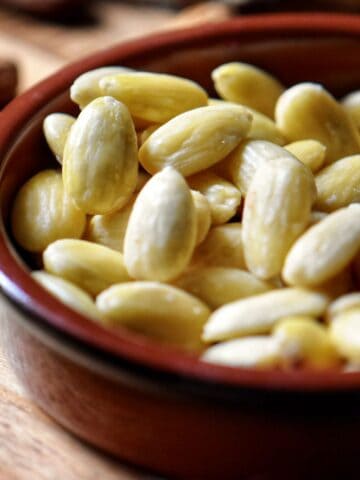 Blanched almonds in a brown ceramic dish.
