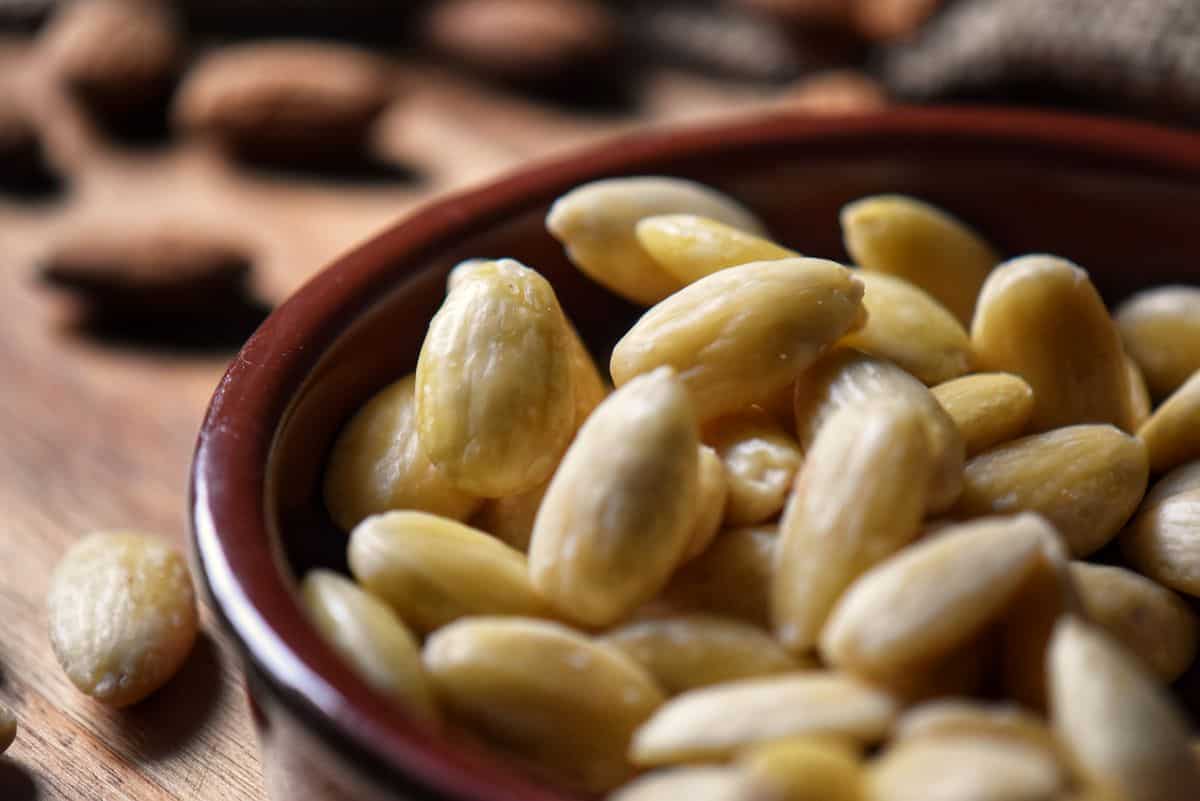 Round dish of blanched almonds with a few almonds on the side.