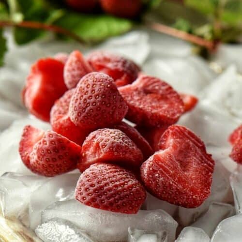 A close up of icy cold frozen strawberry halves set on ice.
