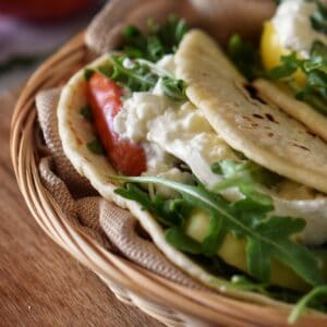 An Italian Piadina Sandwich filled with arugula, tomatoes and burrata cheese.
