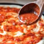 A wooden spoon with homemade pizza sauce garnishing a pizza.