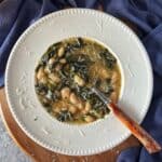 An overhead photo of white beans and spinach soup on a white bowl with a tablespoon.